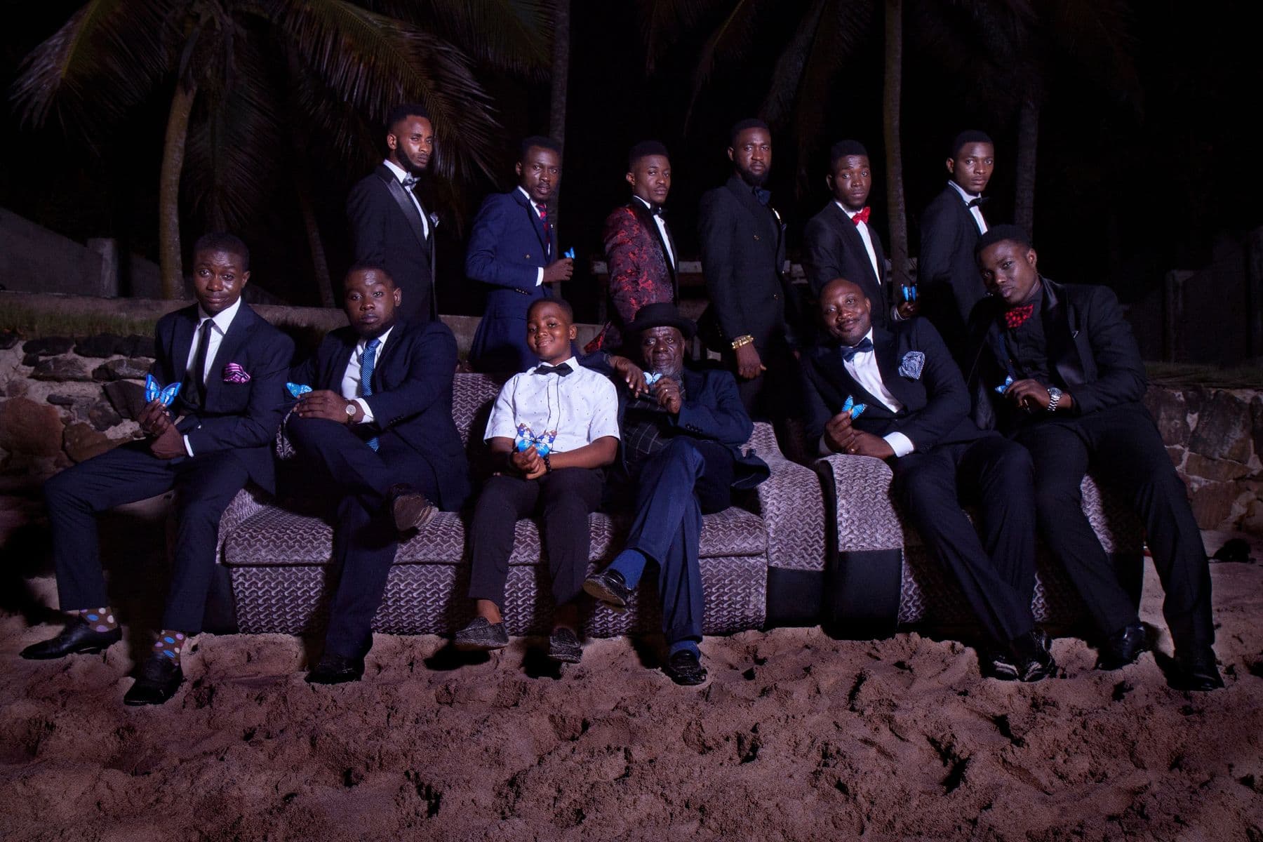 A group of men in dark suits seated on a sofa on a beach at night