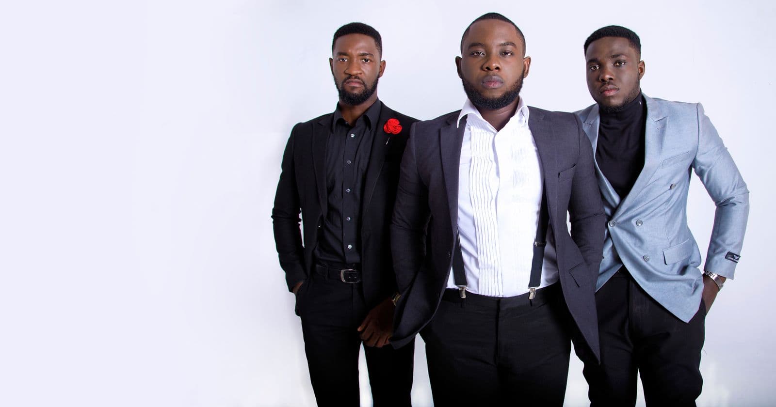 Three men in dark clothes posing in a white studio