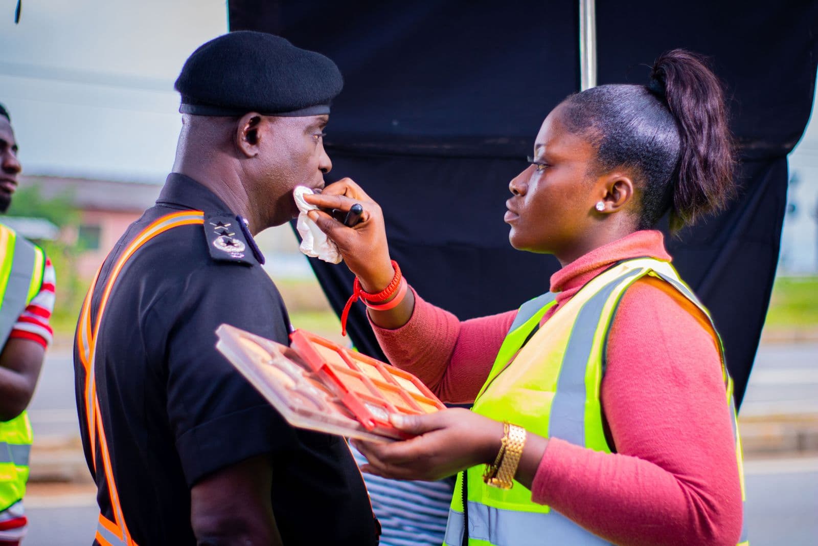 A make-up artist touching up an actor in police uniform