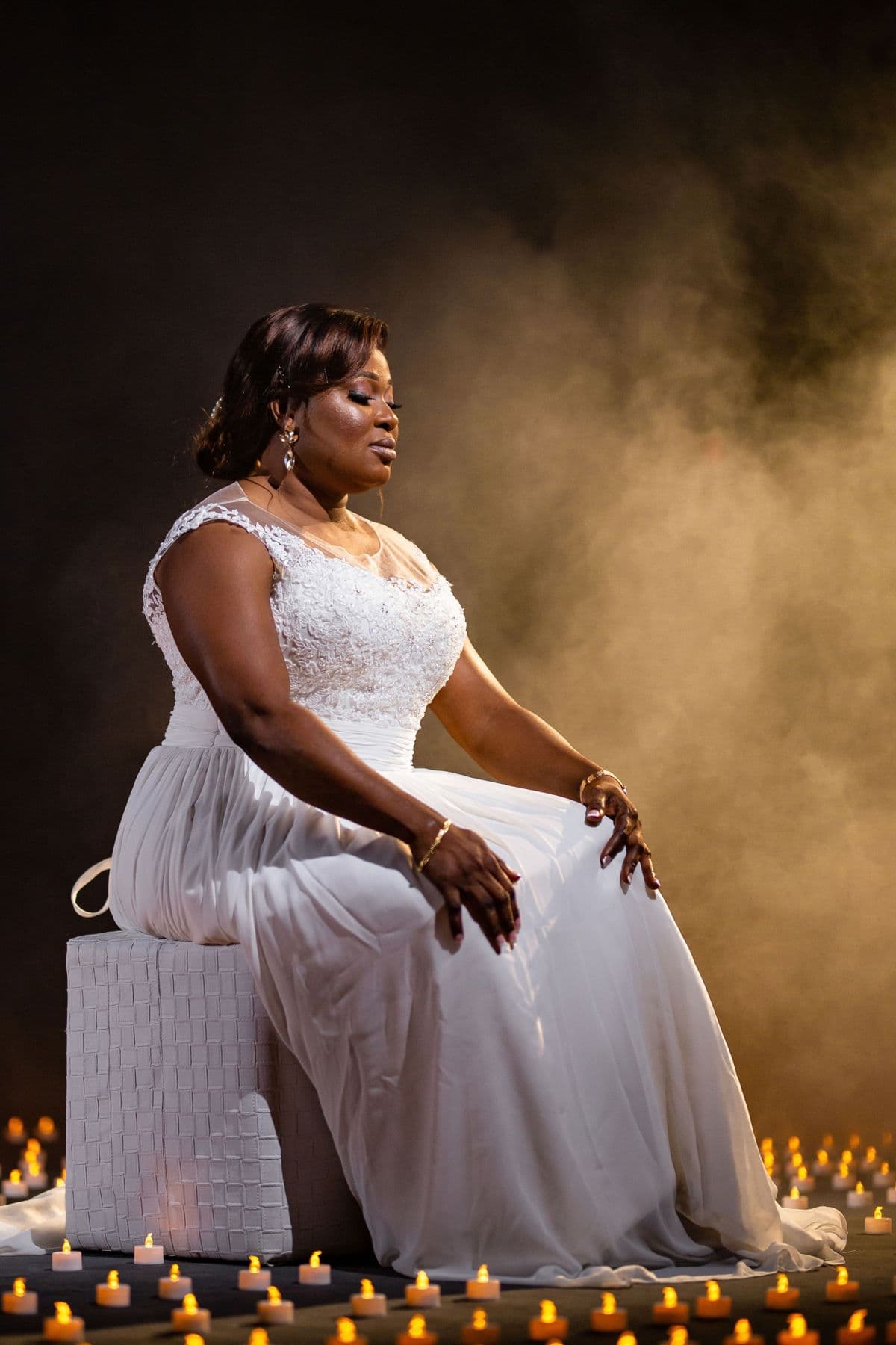 The singer in a white gown, seated among candles in drifting smoke