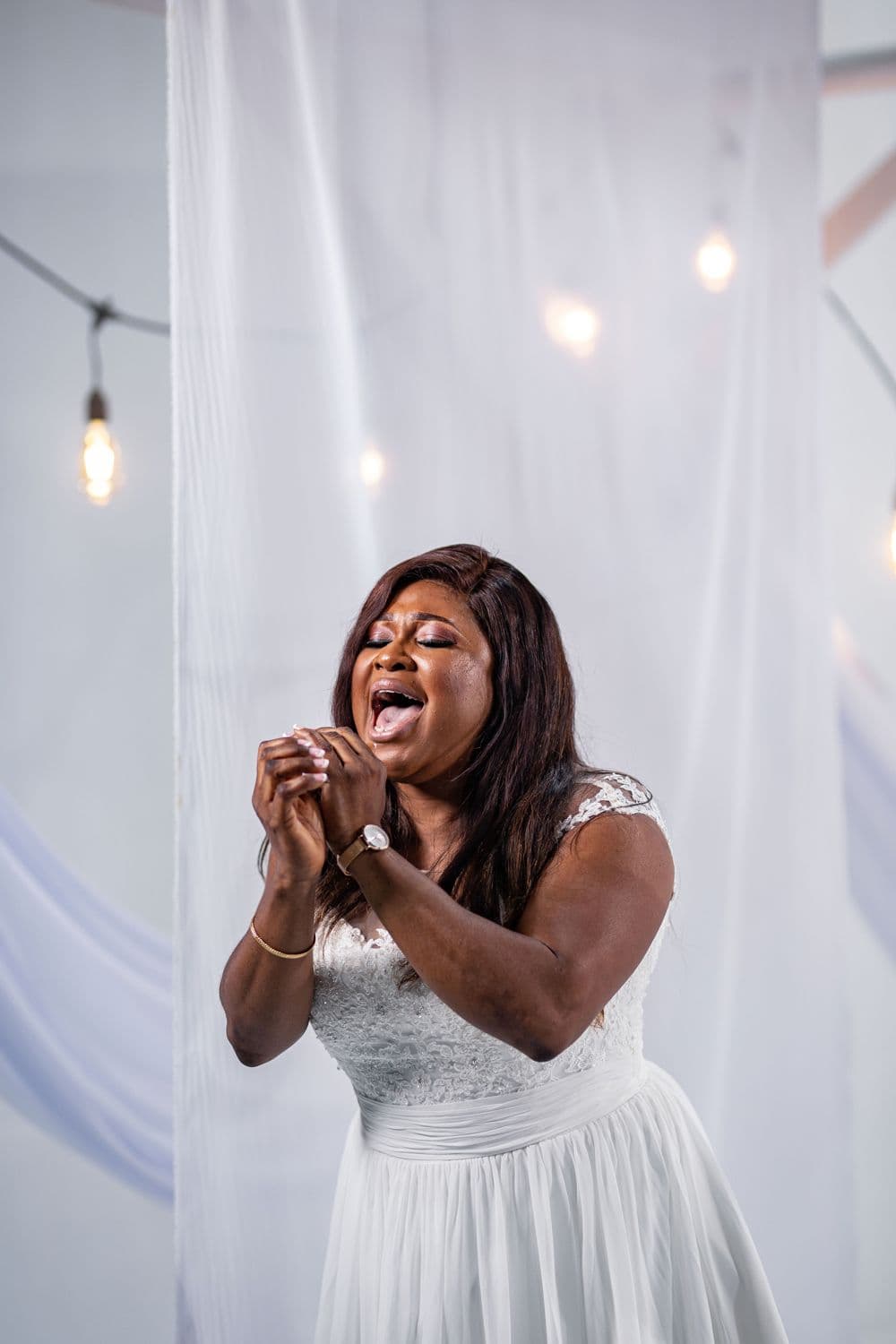 The singer in white before a sheer curtain and string lights