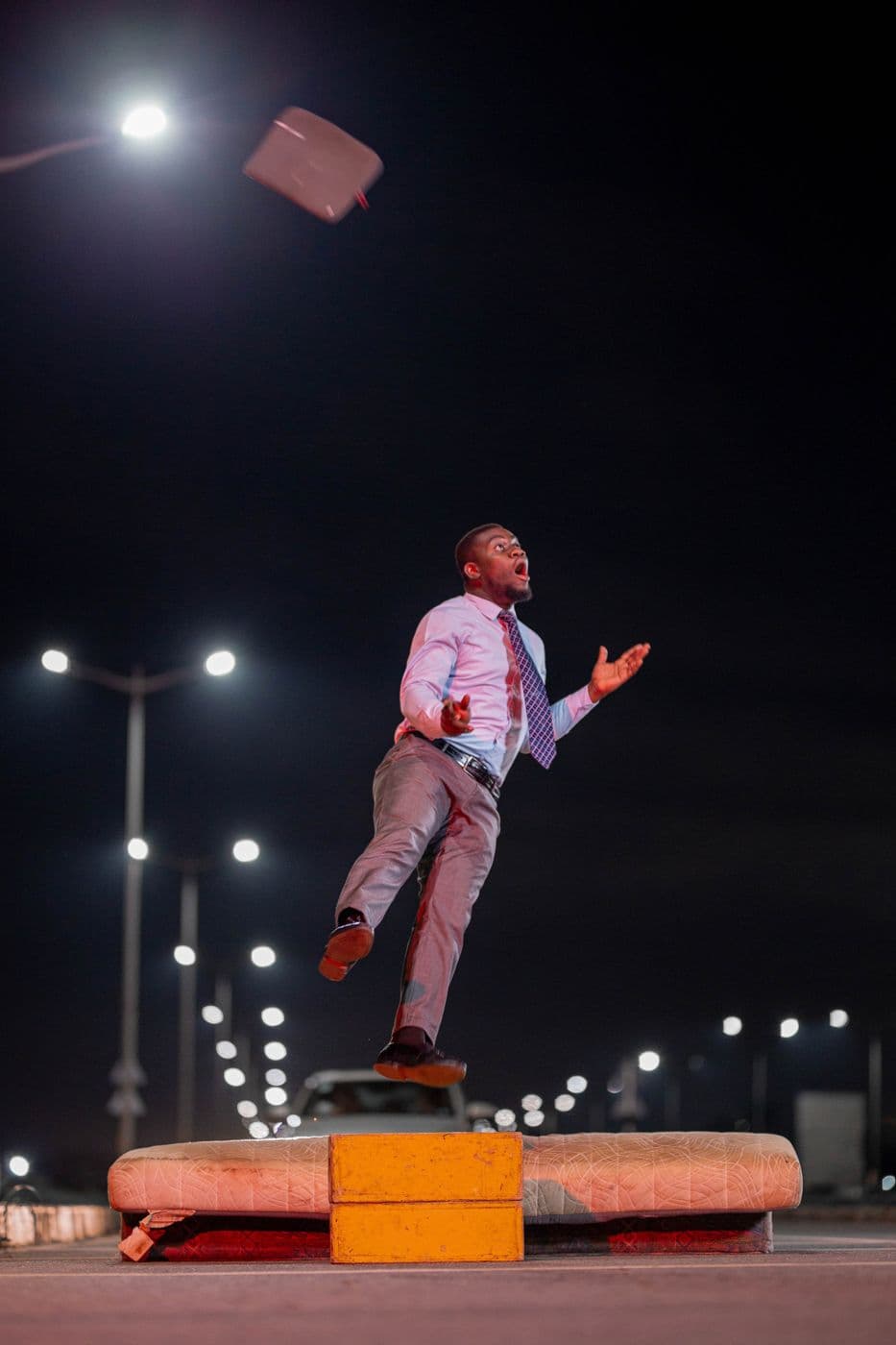 A man leaping on a lit road at night, under street lamps