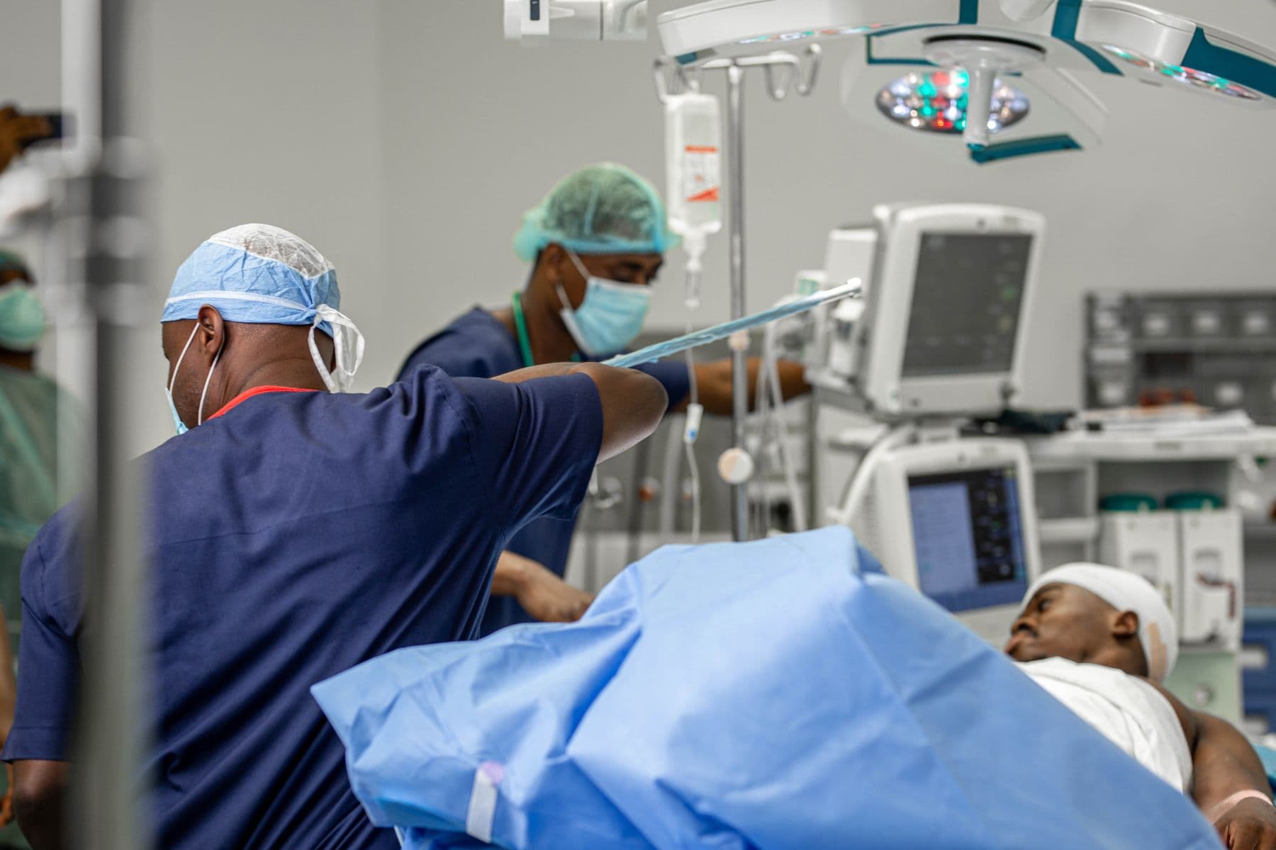 An operating theatre with a patient under a blue drape and staff in scrubs