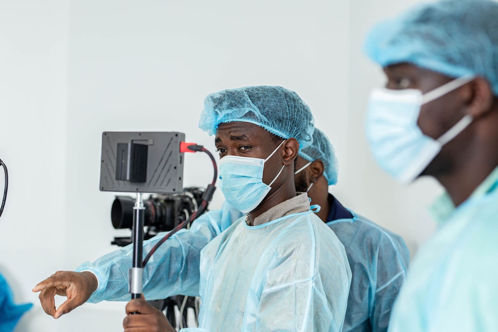 A camera operator in a surgical cap and mask watching a monitor