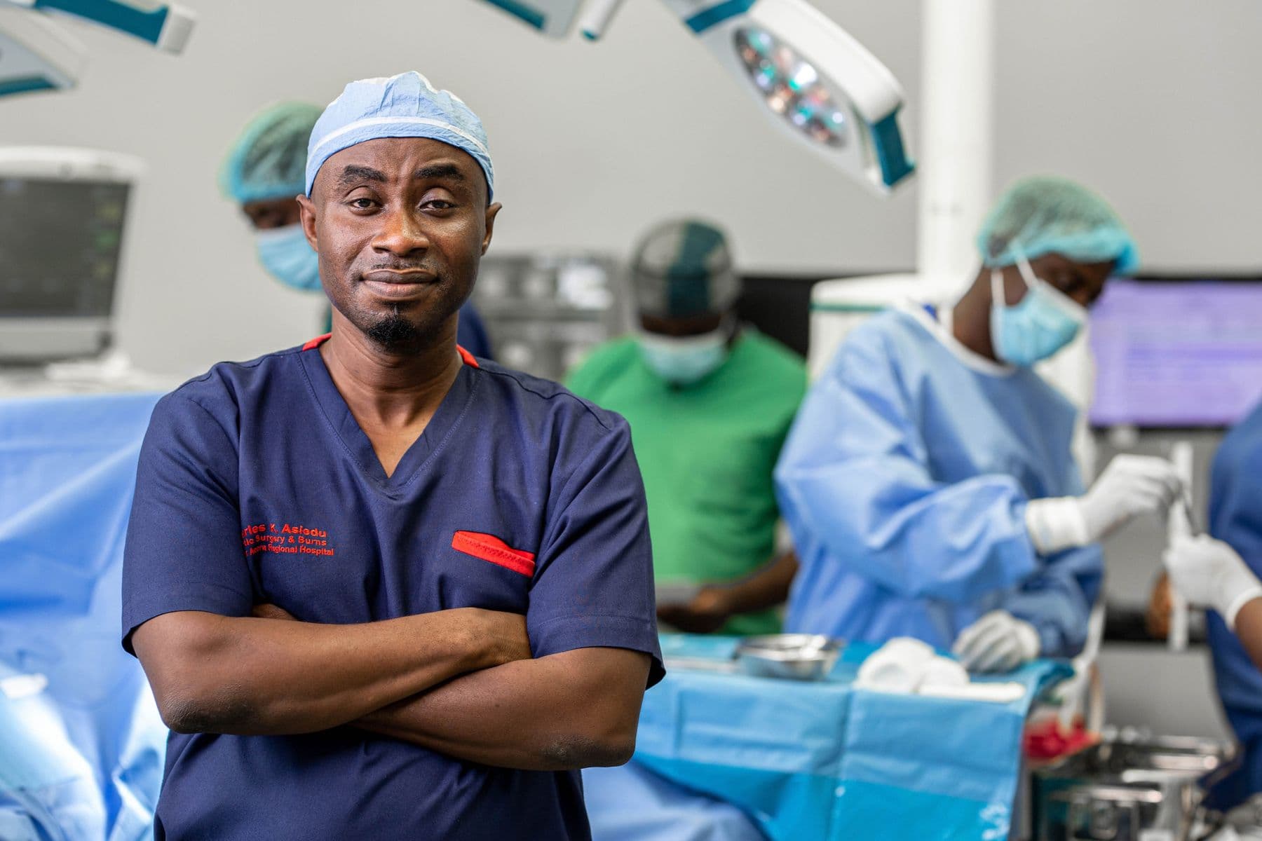 A surgeon in scrubs with arms folded, in an operating theatre