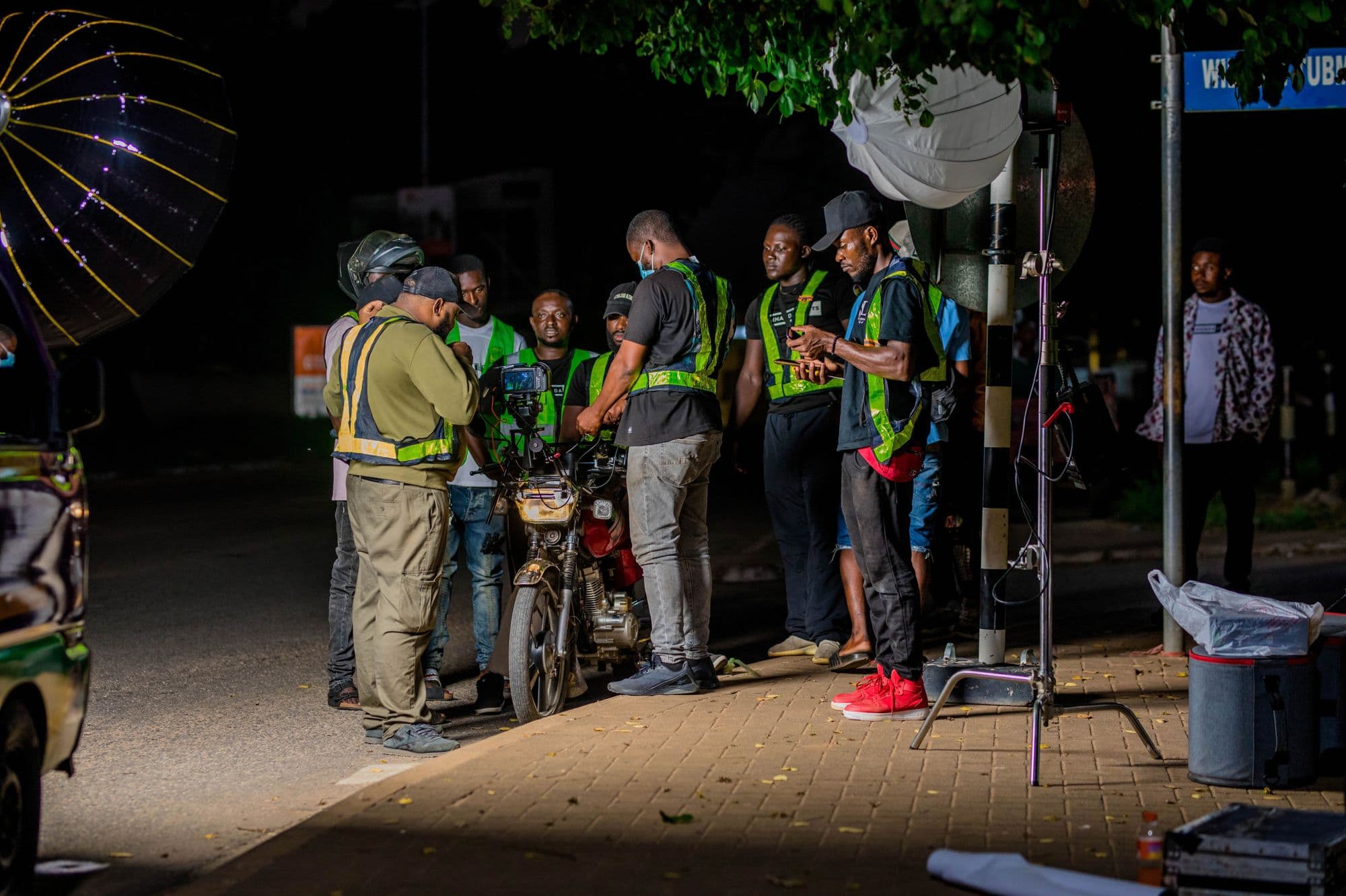 A crew working on a street at night, lit by stands and a round reflector