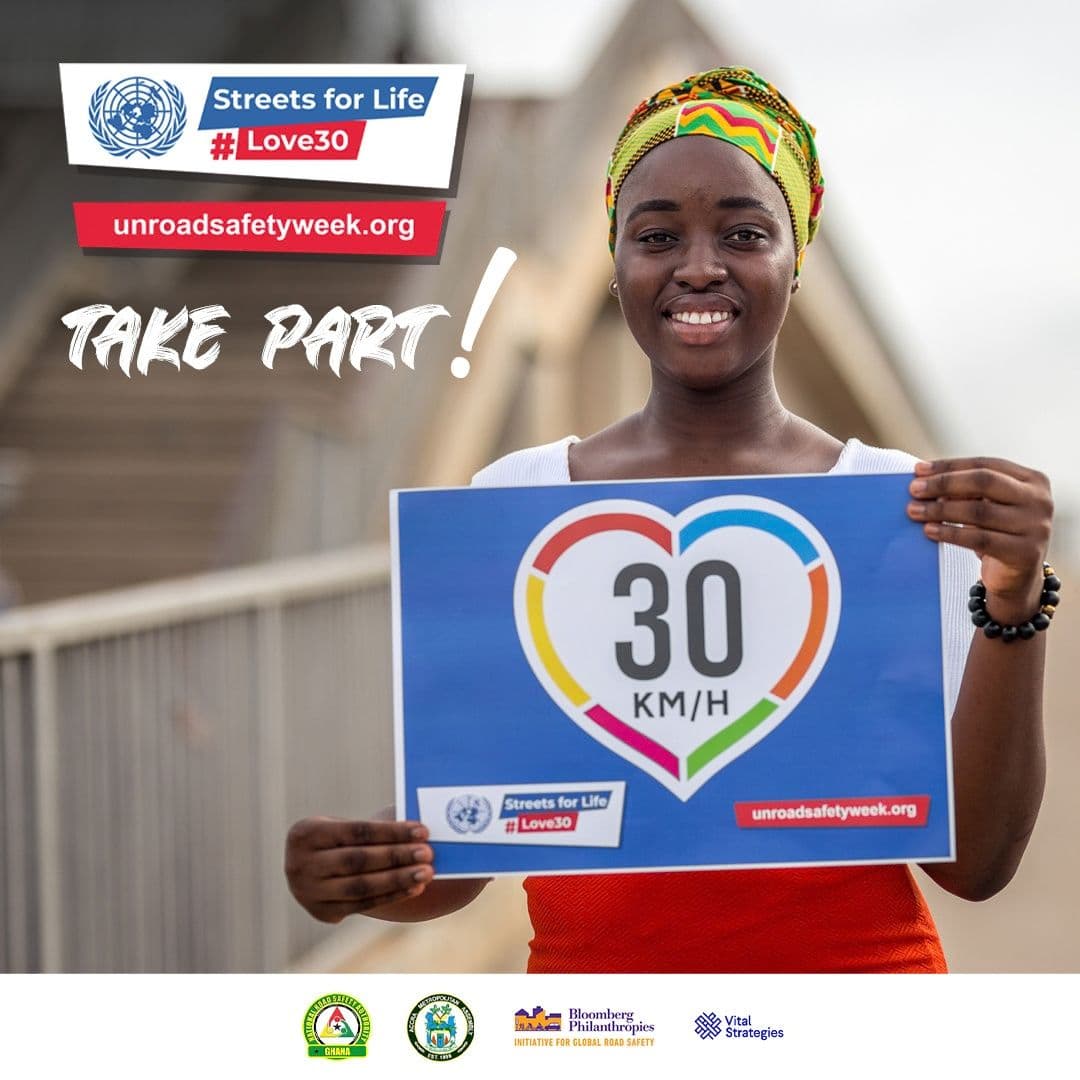 A smiling woman in a yellow headwrap holding a 30 km/h sign